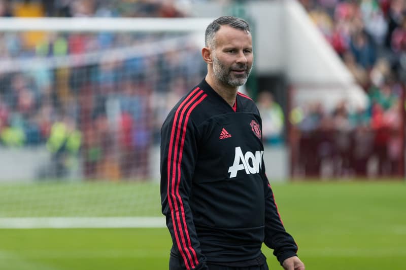 A man, one of the 20 best soccer midfielders of all time, is standing on a field wearing a red shirt.