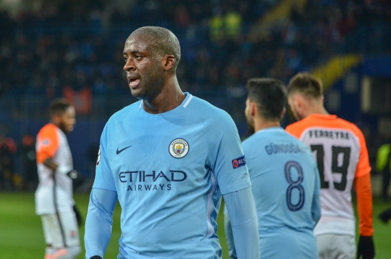 A man in a blue shirt is standing on a soccer field among the 15 strongest soccer players in the world.